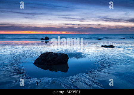 Rock in a tidal pool on the beach at dusk, Church Bay, Anglesey, North Wales Stock Photo