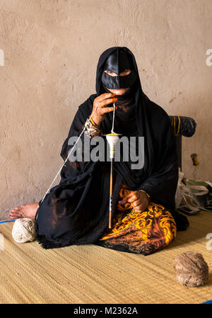 Nizwa, Oman, Febrary 2nd, 2018: old woman in full traditional outfot, spinning yarn Stock Photo
