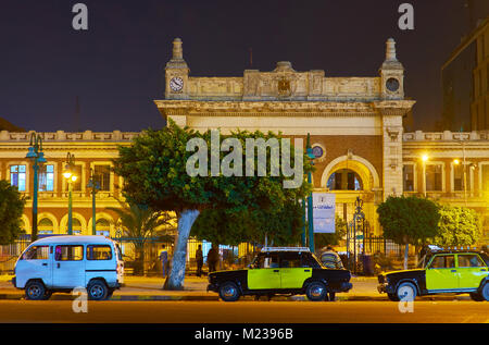 ALEXANDRIA, EGYPT - DECEMBER 17, 2017: The facade of historic building of Misr Railway Station, located in old town with black-yellow taxi cars on for Stock Photo