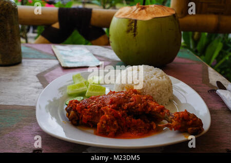 Typical Indonesian Dish: Nasi Ayam Plecing (Chicken with rice and special sauce) and young coconut. Stock Photo