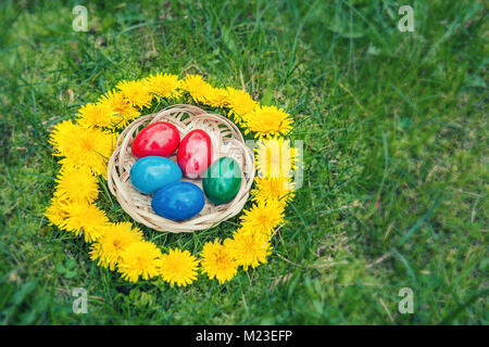 Easter eggs in basket on a grass lawn in a wreath from dandelions. Stock Photo