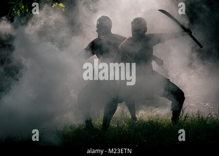 AYUTTHAYA, THAILAND - DECEMBER 17: Two ancient swordmen  be ambush alert in the smoke of war fire make more shadow and Silhouette and prepare for atta Stock Photo