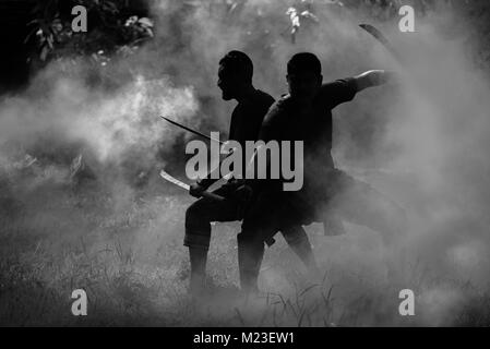AYUTTHAYA, THAILAND - DECEMBER 17: Two ancient swordmen  be ambush alert in the smoke of war fire make more shadow and Silhouette and prepare for atta Stock Photo