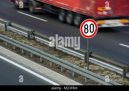 Traffic sign showing 80 km/h speed limit on a highway with red truck driving in the background Stock Photo