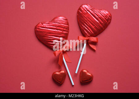 Heart shaped, foil wrapped chocolate lollipops on a red background with copy space Stock Photo