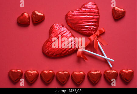 Heart shaped, foil wrapped chocolate lollipops on a red background with copy space Stock Photo