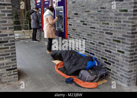 Person sleeping rough next to Natwest ATM cash machines in London, England, United Kingdom, UK
