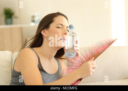 Stressed girl suffering a heatstroke refreshing with a fan sitting on a couch in the living room at home Stock Photo