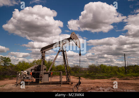 A dramatic sky surrounds this oil pump jack in a muddy bog in the united states Stock Photo