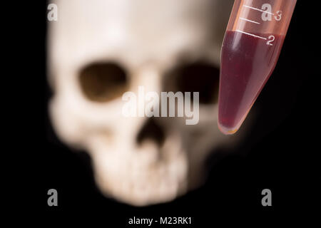 blood sample or other red liquid in testtube and blurry skull isolated on black background Stock Photo
