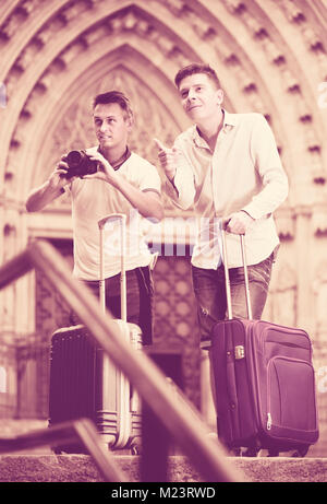 Smiling  males standing with baggage at street and taking photos Stock Photo