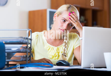 Tired female manager doing routine paperwork at the table in office Stock Photo