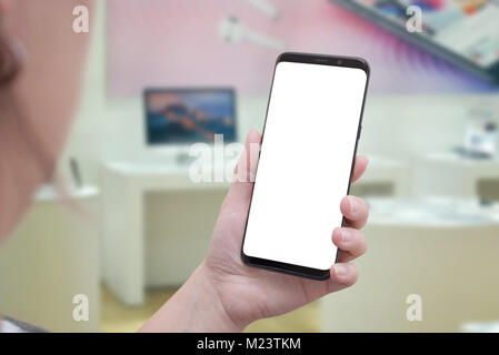 Use mobile phone in office. Isolated screen for mockup. Computers and desks in background. Stock Photo