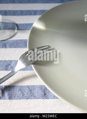 Fork resting on an empty white plate on a blue white table cloth and glass Stock Photo