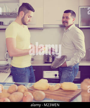 Smiling father and son cooking potato soup indoors. Focus on the right man Stock Photo