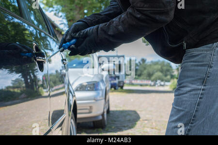 A person with gloves is trying to break the lock of a car on a street Stock Photo