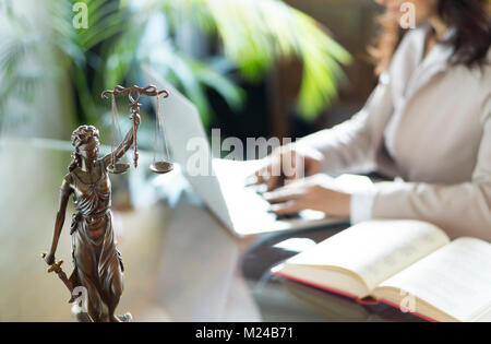 Lawyer office. Statue of Justice with scales and lawyer working on a laptop. Legal law, advice and justice concept Stock Photo