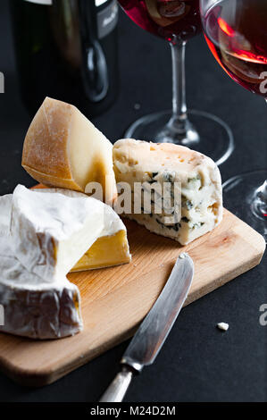 Assortment of cheeses  on a wooden plate with vintage silver knife and two glasses of red wine. Vertical. Stock Photo