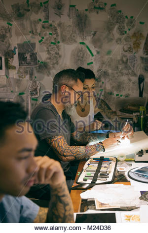 Tattoo artist brainstorming, sketching at light table in tattoo studio office
