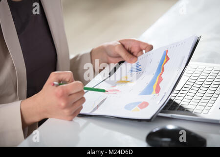 Close-up Of A Businesswoman's Hand Holding Graph And Pencil Over The Desk At Workplace Stock Photo
