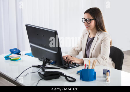 A Happy Young Businesswoman Wearing Eyeglasses Typing On Keyboard In Office Stock Photo