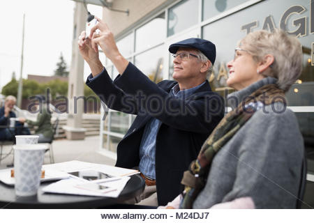 Senior couple using camera phone at sidewalk cafe