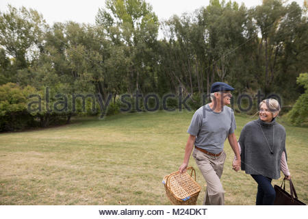 Smiling senior couple walking and holding hands, carrying picnic basket in park