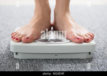 Close-up Of A Woman's Feet On Weighing Scale Over The Carpet Stock Photo
