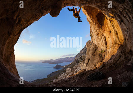 Young man lead climbing on ceiling in cave, just before sunset Stock Photo