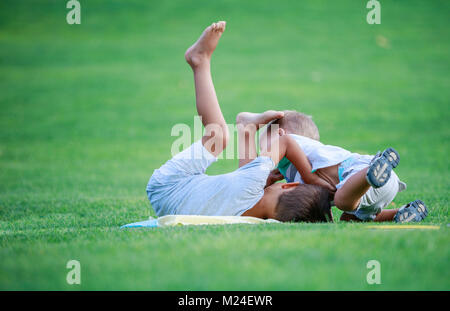 Two boys fighting outdoors. Siblings wrestling on grass in summer park. Siblings rivalry. Stock Photo