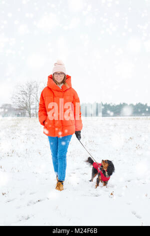 Full length shot of a happy woman walking her small dog outdoor in winter. Stock Photo