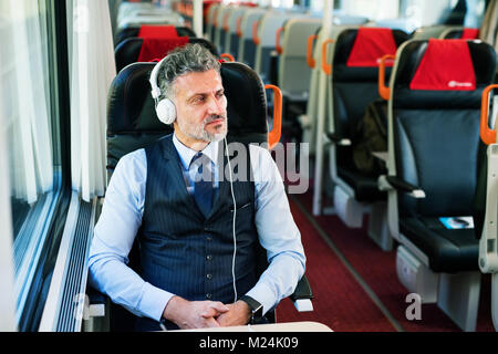 Mature businessman with headphones travelling by train. Stock Photo
