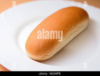 Closeup of a soft plain hot dog bun on a white plate. Stock Photo