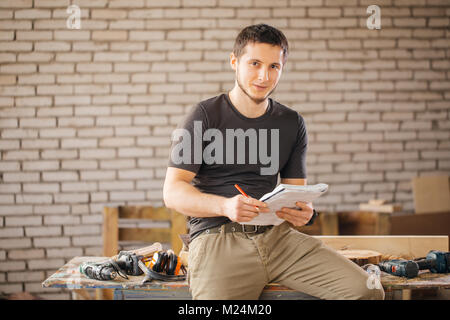 Man carpenter in his home studio draws sketches in pencil in notebook Stock Photo