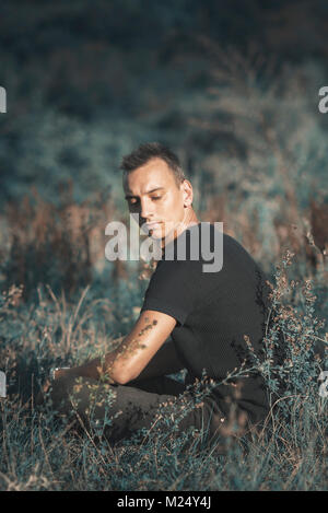 Sad man sitting alone in an empty field Stock Photo