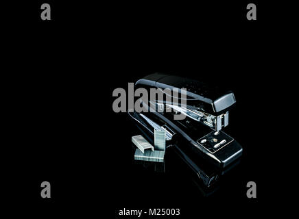 Black stapler and staples on dark background. Stock Photo