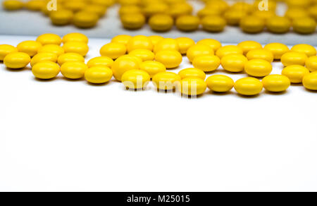 Macro shot detail of yellow round sugar coated tablets pills on blurred tablets pills background with copy space for text. Stock Photo
