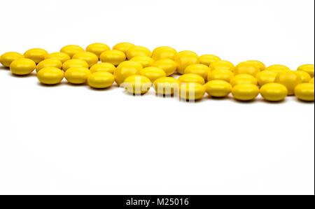 Macro shot detail of yellow round sugar coated tablets pills on white background with copy space for text. Stock Photo
