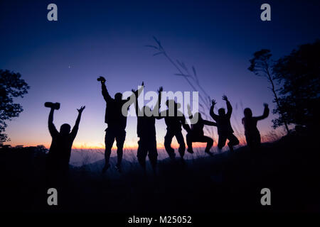 Happy friends, family jumping together in a circle having fun and expressing emotions of joy, freedom, success. Silhouettes on sunny sky Stock Photo
