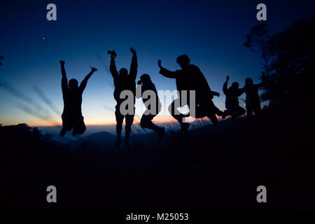 Happy friends, family jumping together in a circle having fun and expressing emotions of joy, freedom, success. Silhouettes on sunny sky Stock Photo