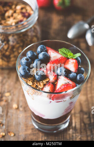 Yogurt with baked granola and berries in white ceramic plate on wooden ...