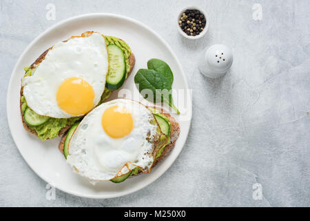 Two toasts with avocado, cucumber and egg on white plate over grey concrete background. Top view with copy space for text Stock Photo