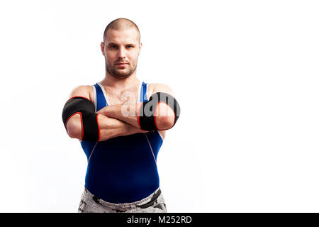 Young sportive man in blue tights and black elbow stands and holds his hands cross-over on his chest on a white isolated background Stock Photo