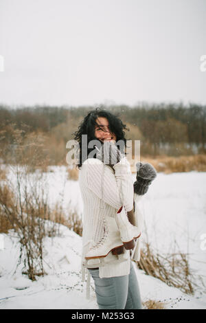 Smiling woman with a pair of ice skates over a shoulder and windswept hair Stock Photo