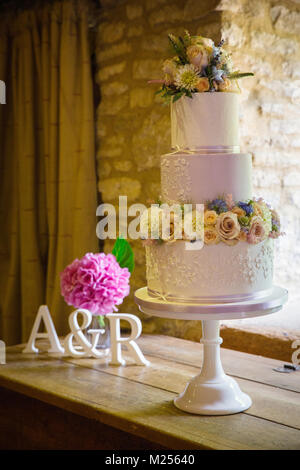 Fresh flowers on three tiered wedding cake on cake stand Stock Photo