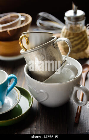 Stack of old different cups and mugs with kitchen utensils on background Stock Photo