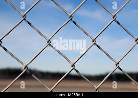 Close up of a chain linked fence with a blurred blue sky landscape on the background. Stock Photo