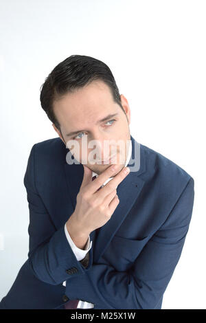 A well dressed confident man in a suit has his hand on his chin looking thoughtful at the camera isolated on a white background Stock Photo