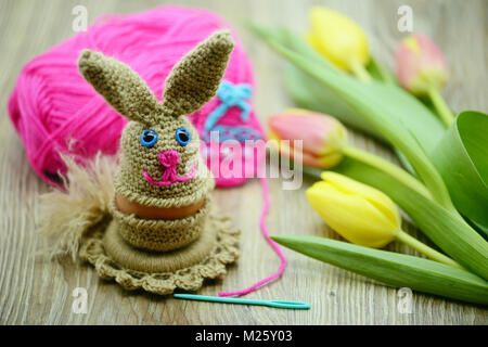 Crochet Easter bunny egg cup made of wool. fresh tulips and wool ball in background Stock Photo