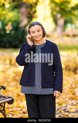 Positive senior woman talking on smartphone outdoors in park. Stock Photo